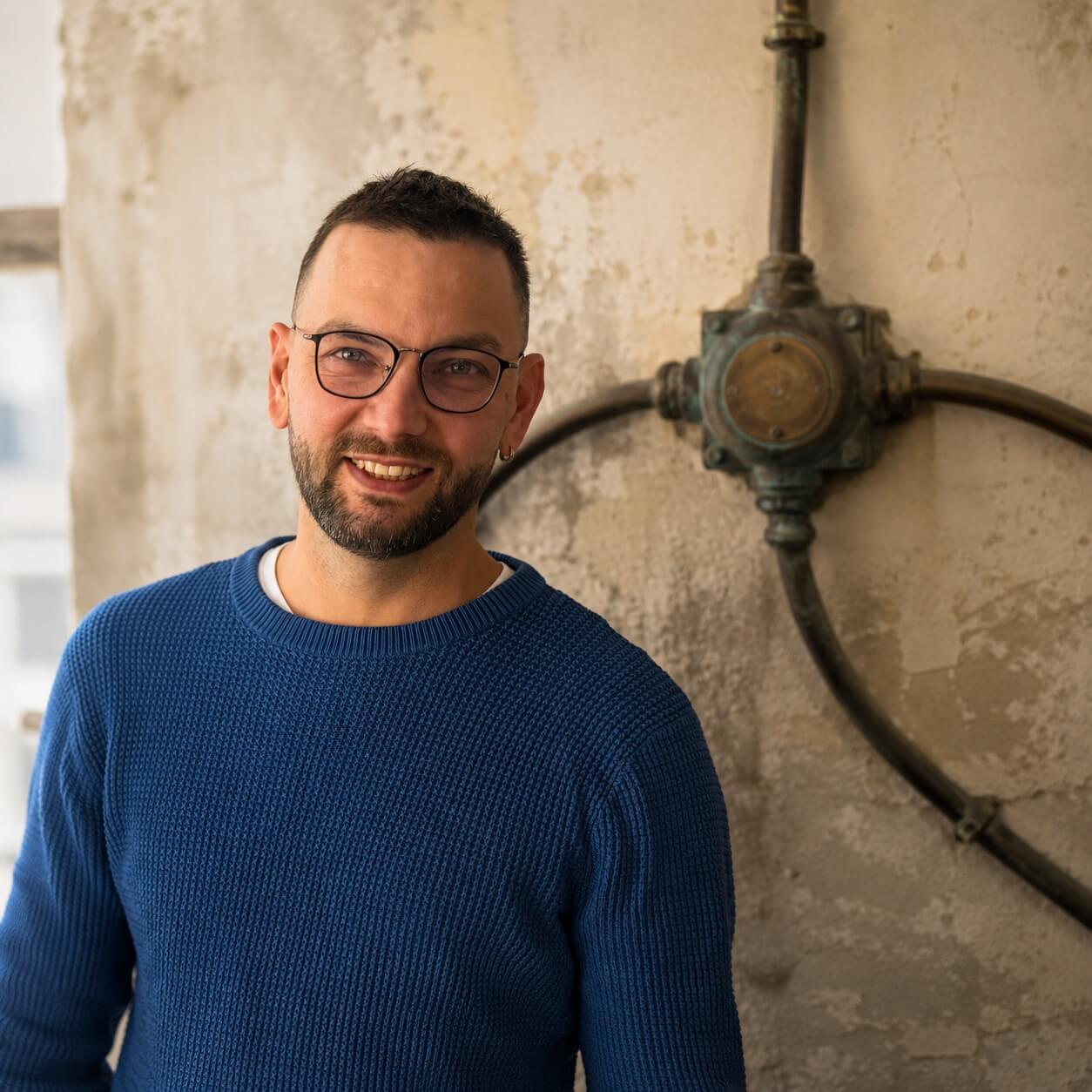 Dennis H&uuml;ttner, Gr&uuml;nder der Waterproof Web Wizard GmbH, vor einer messingfarbenen Verteilerdose mit abzweigenden Rohren